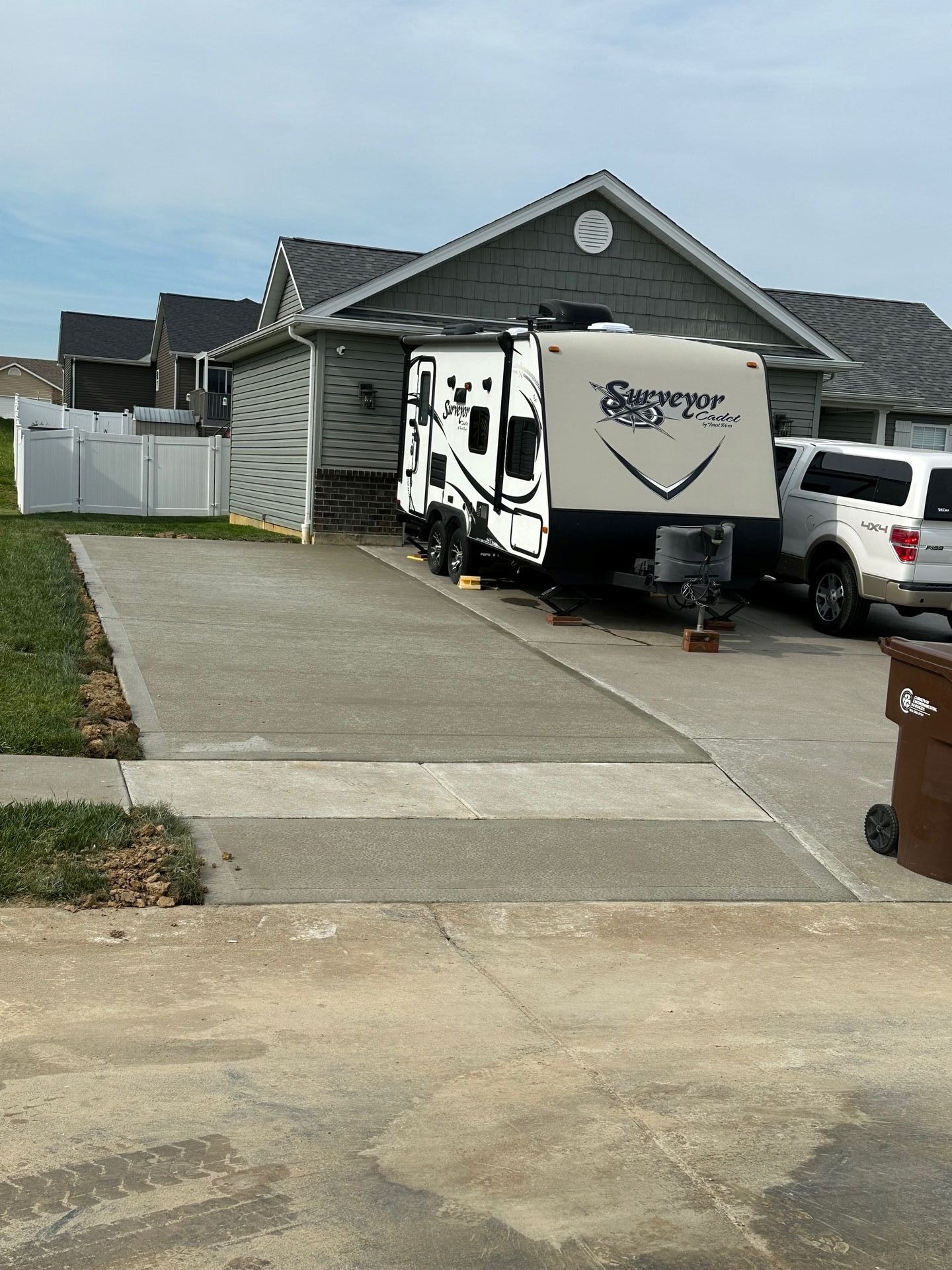 Driveway beside a gray house with a white RV and white SUV parked near the garage.