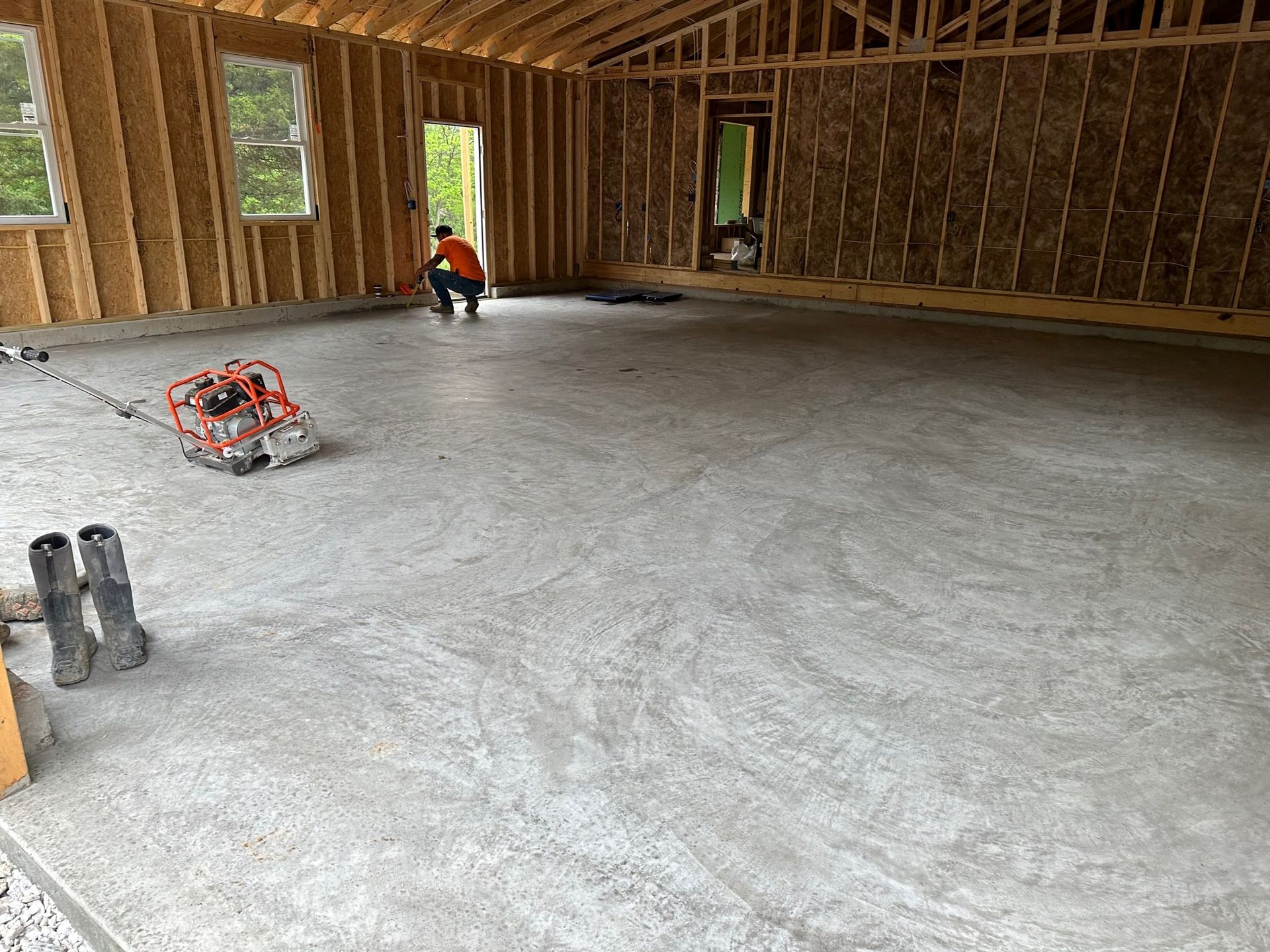 Unfinished framed house interior with concrete floor, exposed studs, and a worker near a window opening