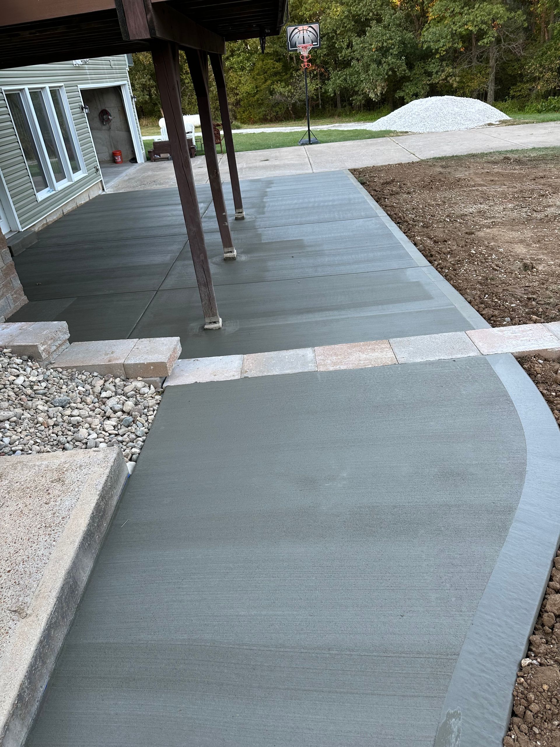 Covered concrete walkway and ramp leading to a building, with gravel borders and porch posts on the left.