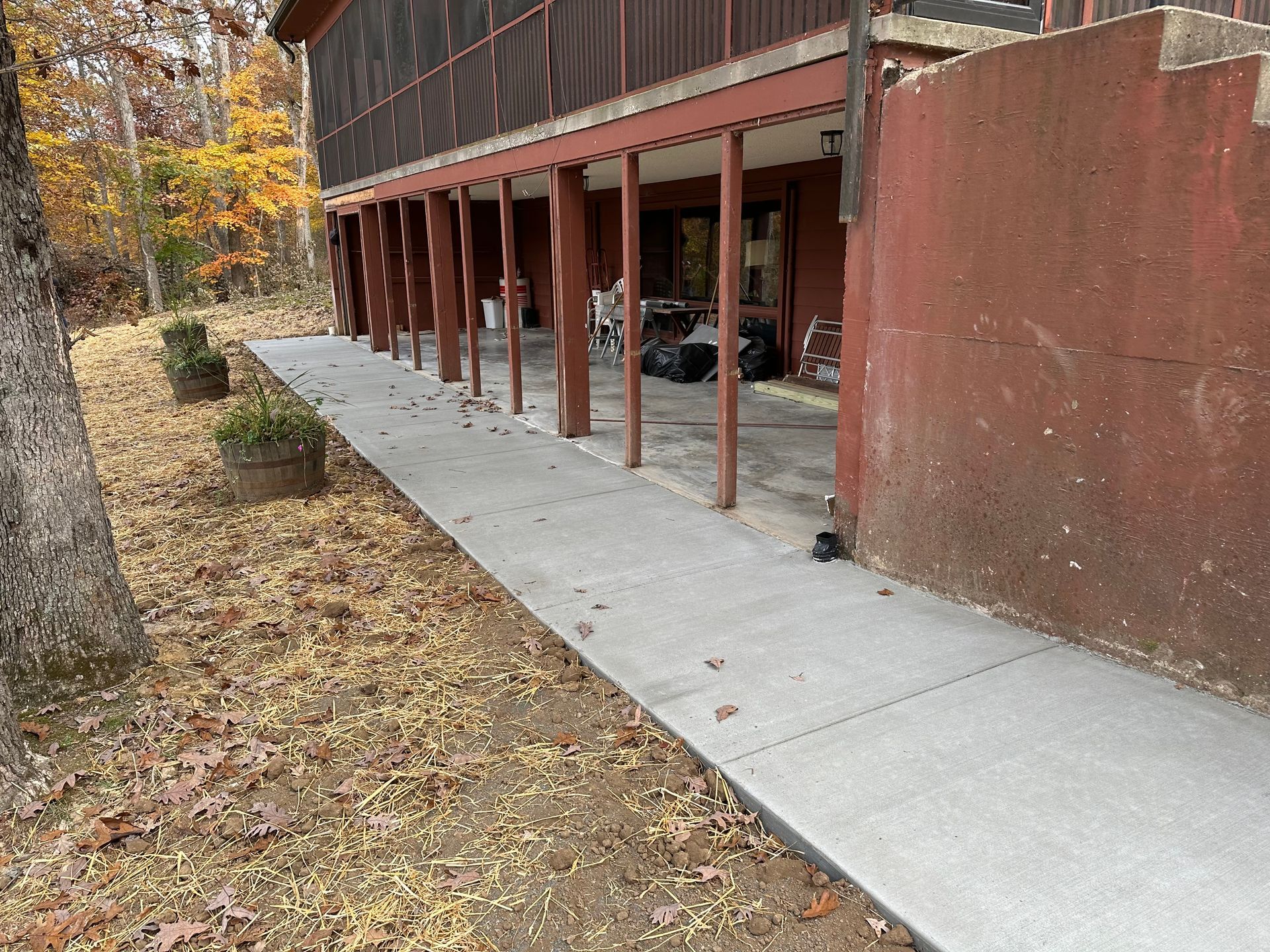 Covered walkway beside a brick building with a concrete sidewalk and autumn leaves on the ground