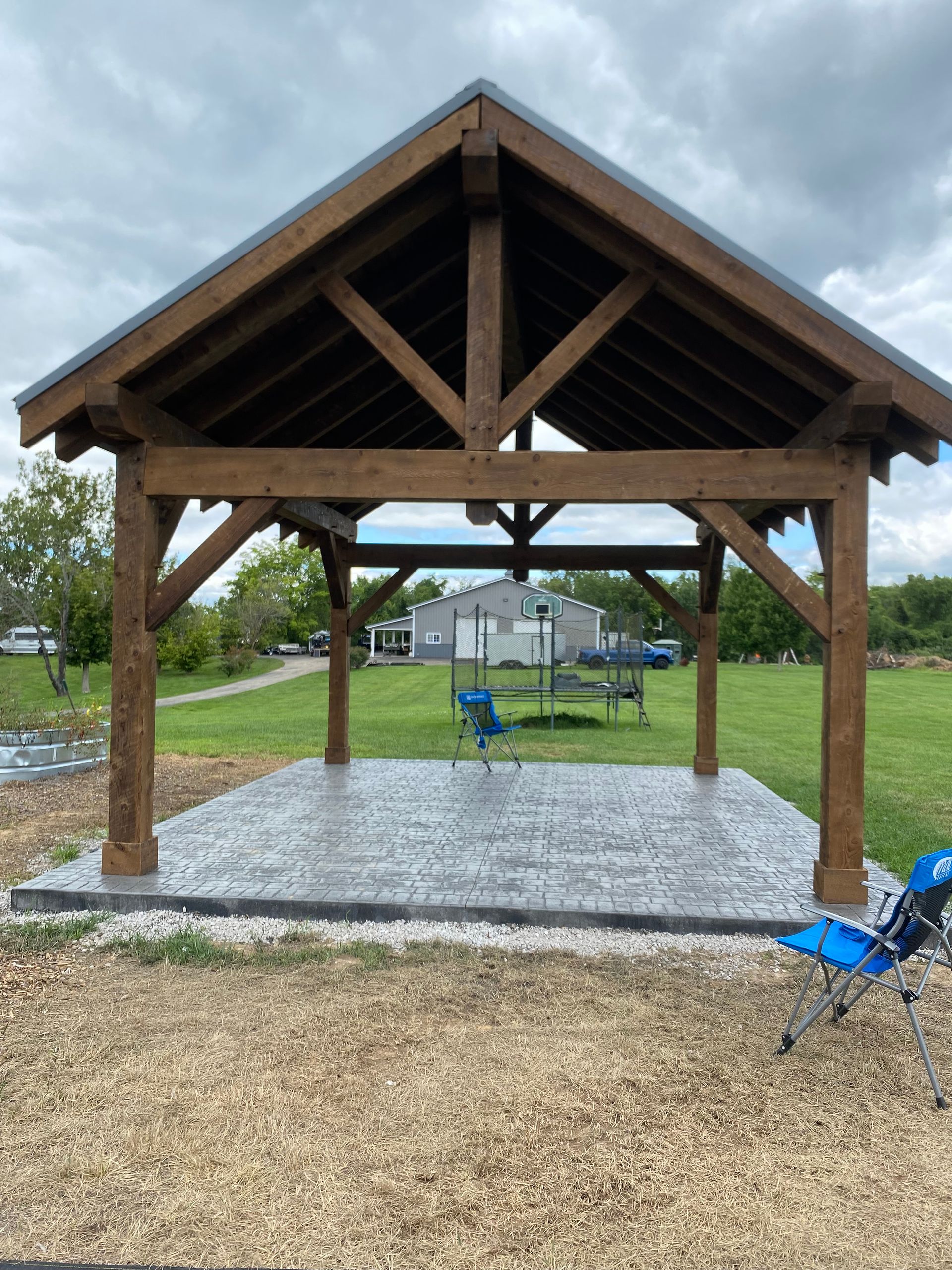 Wooden pavilion with gravel floor in a grassy park, with blue chairs in the background