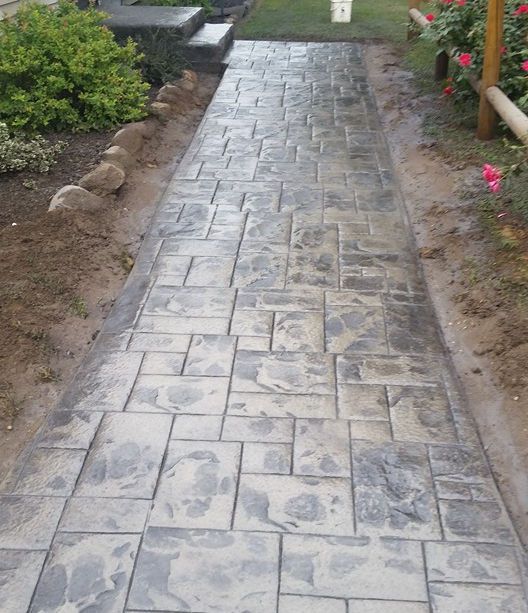 A concrete walkway in a garden with flowers on the side.