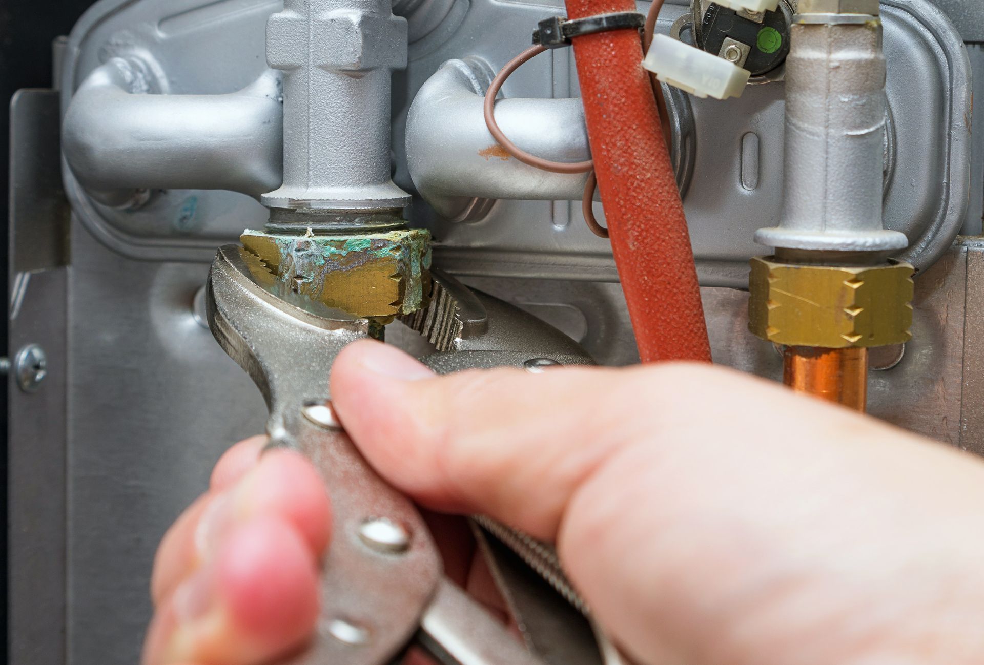 Close-up of hands using a wrench to tighten a brass pipe fitting on plumbing fixtures.