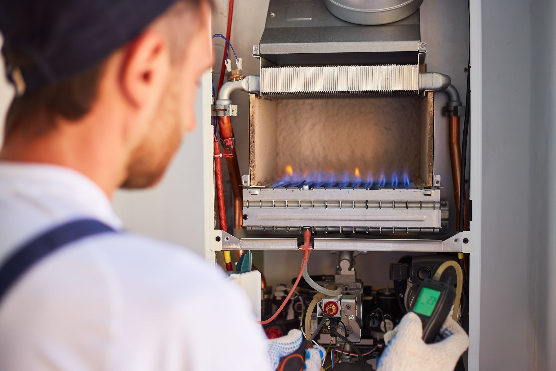 Technician inspecting a gas boiler with a handheld meter and visible blue flames.