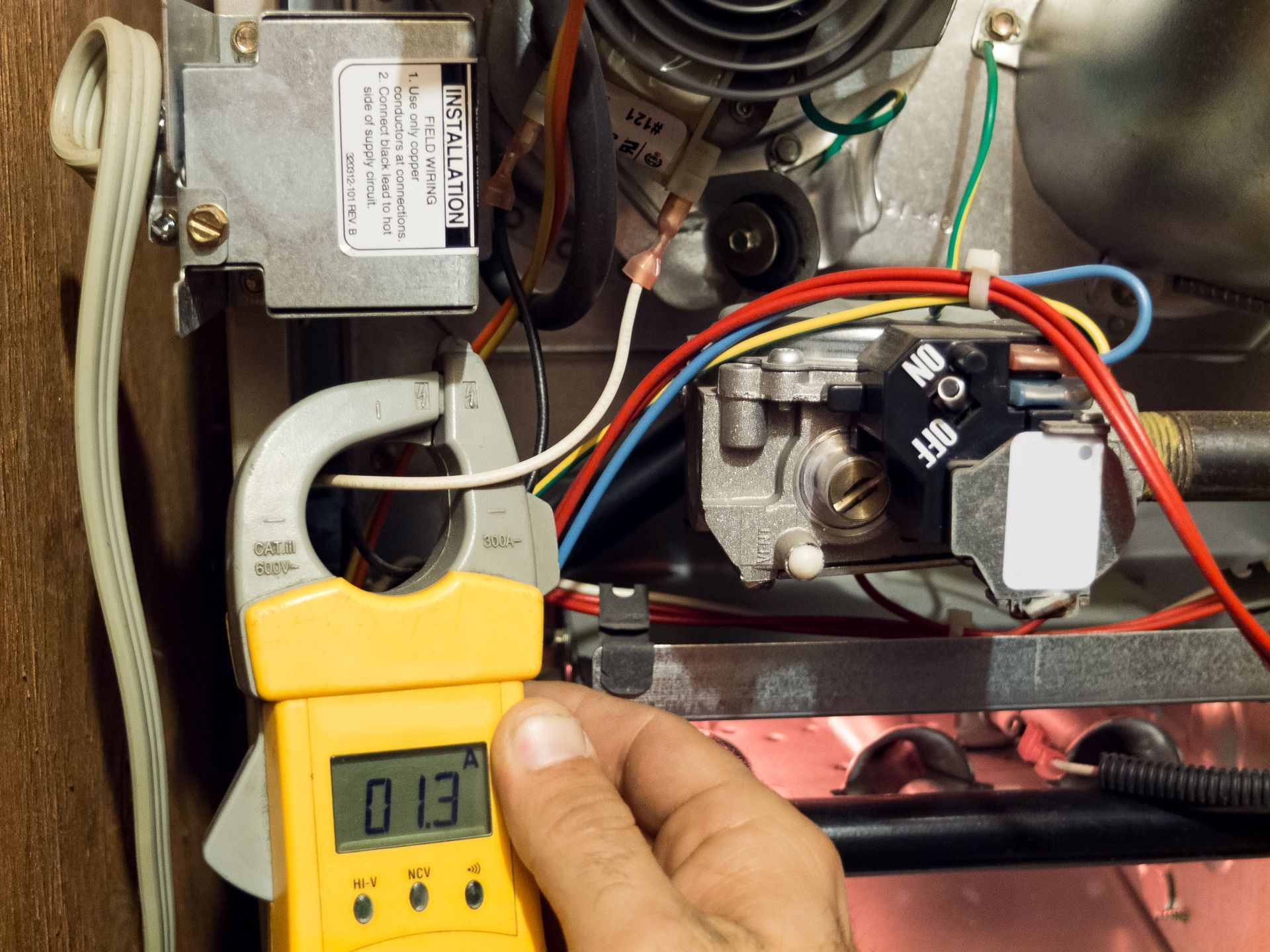 Hand holding a yellow clamp meter measuring wires inside an open electrical appliance