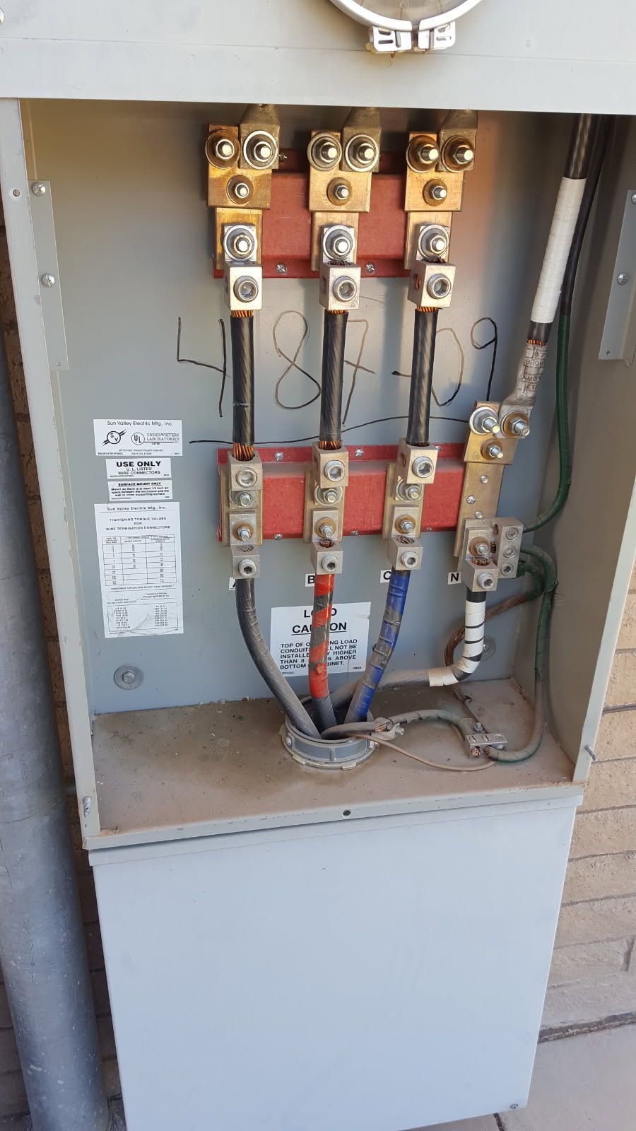 An open electrical meter box mounted on a brick wall, displaying internal wiring, terminal blocks, and colored cables.