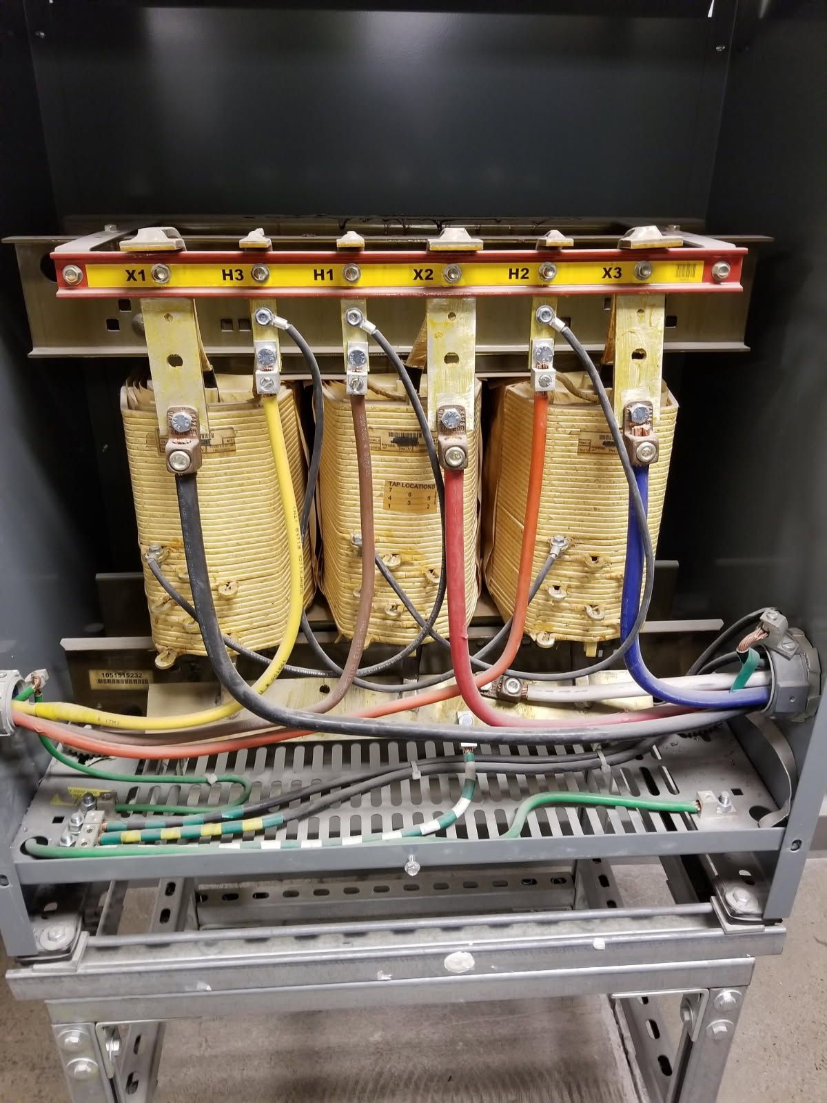 An electrical transformer inside a metal enclosure with colored wires connected to a terminal bus bar.