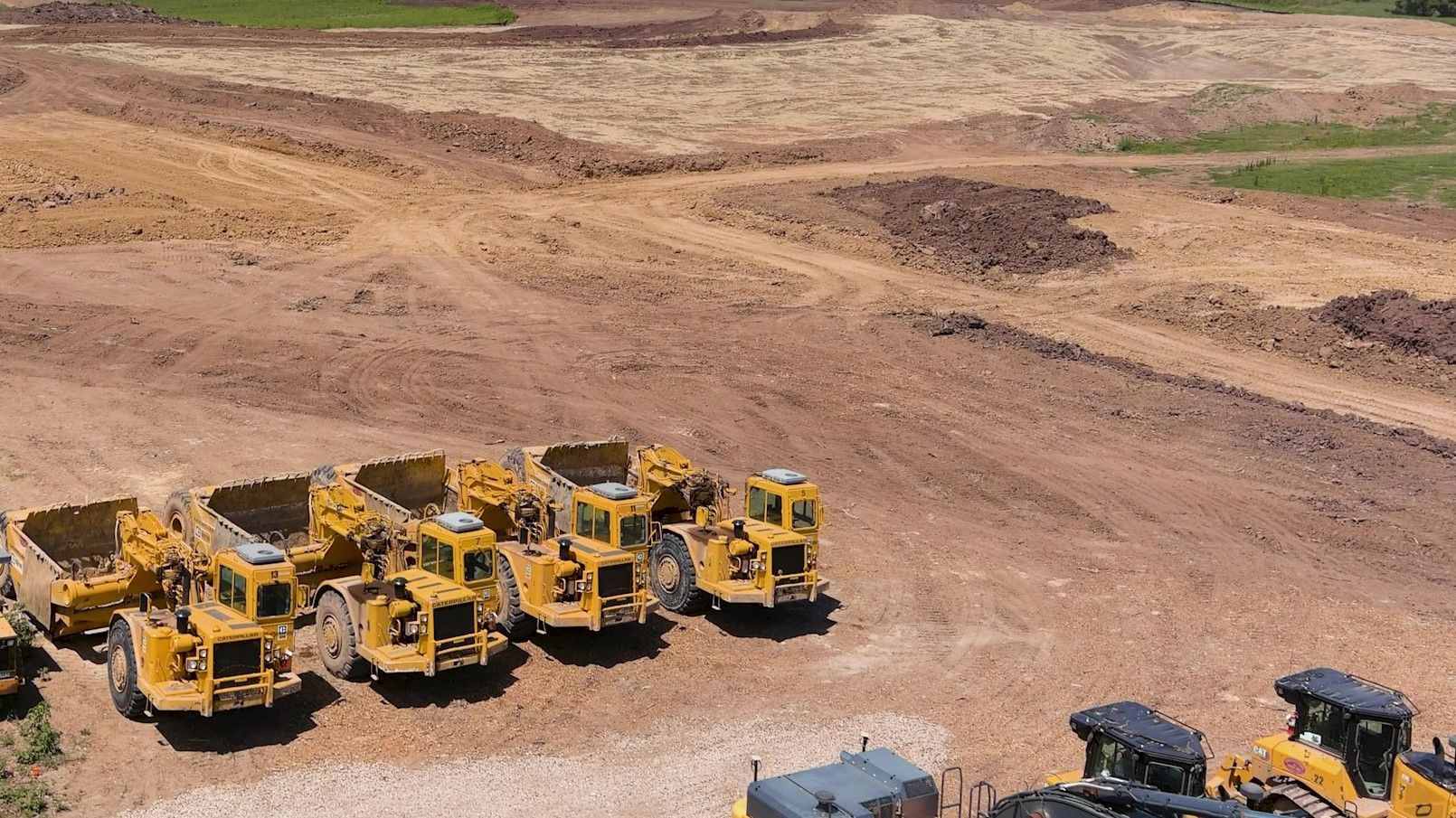 Yellow construction vehicles parked on a dirt lot with recently cleared land in the background.