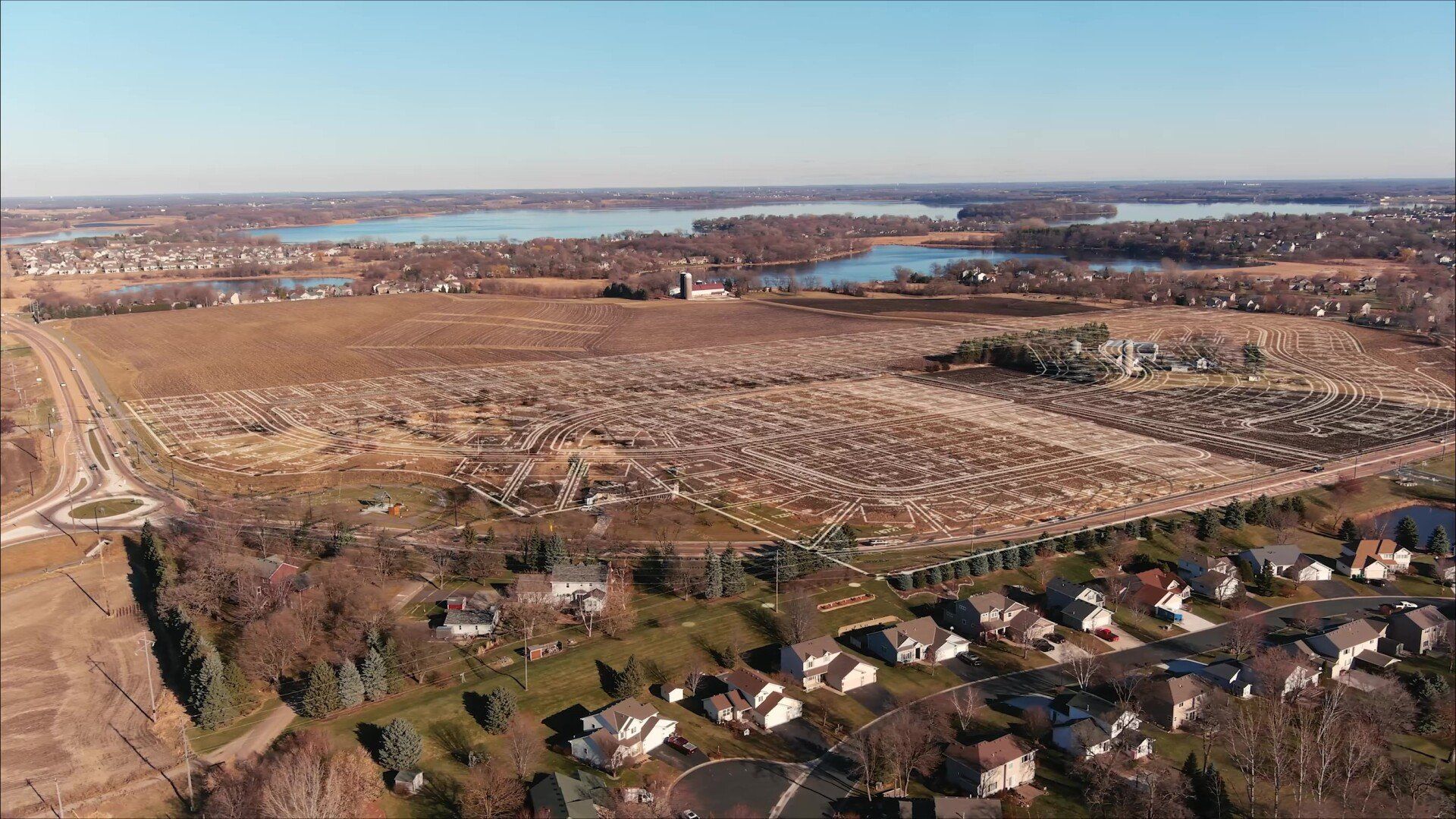Aerial view of a large cemetery with many headstones, a residential area, and several lakes in the distance on a sunny day.