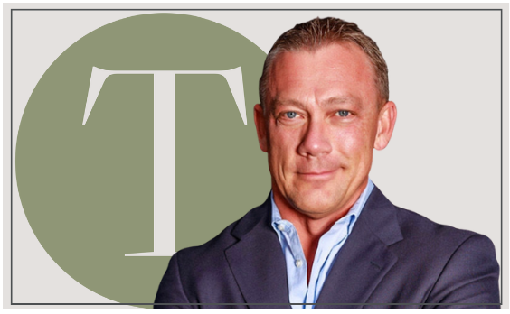 Man in a navy blazer, light blue shirt, with a large green circle and the letter 