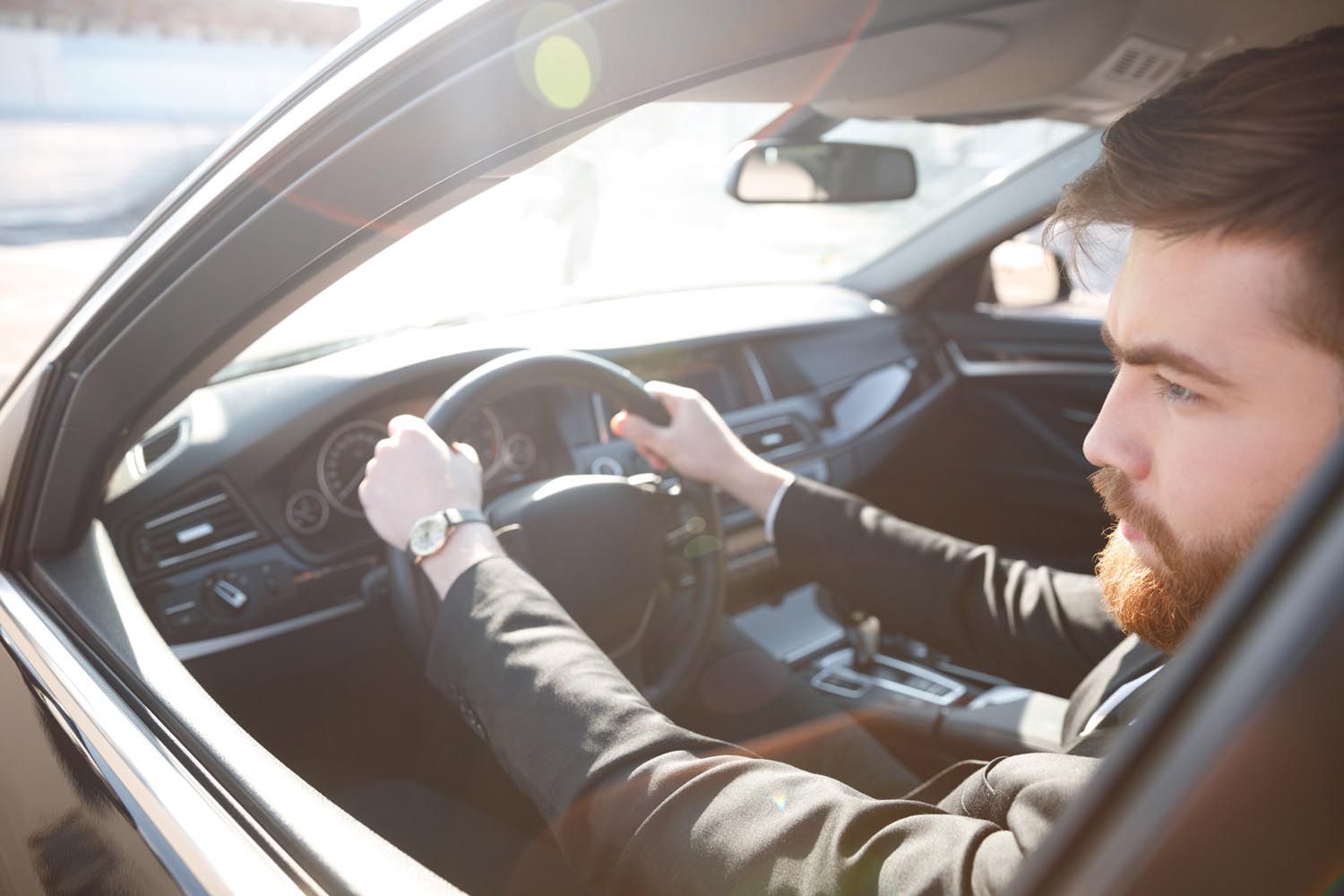 Driver holding the steering wheel inside a car, lit by bright sunlight.