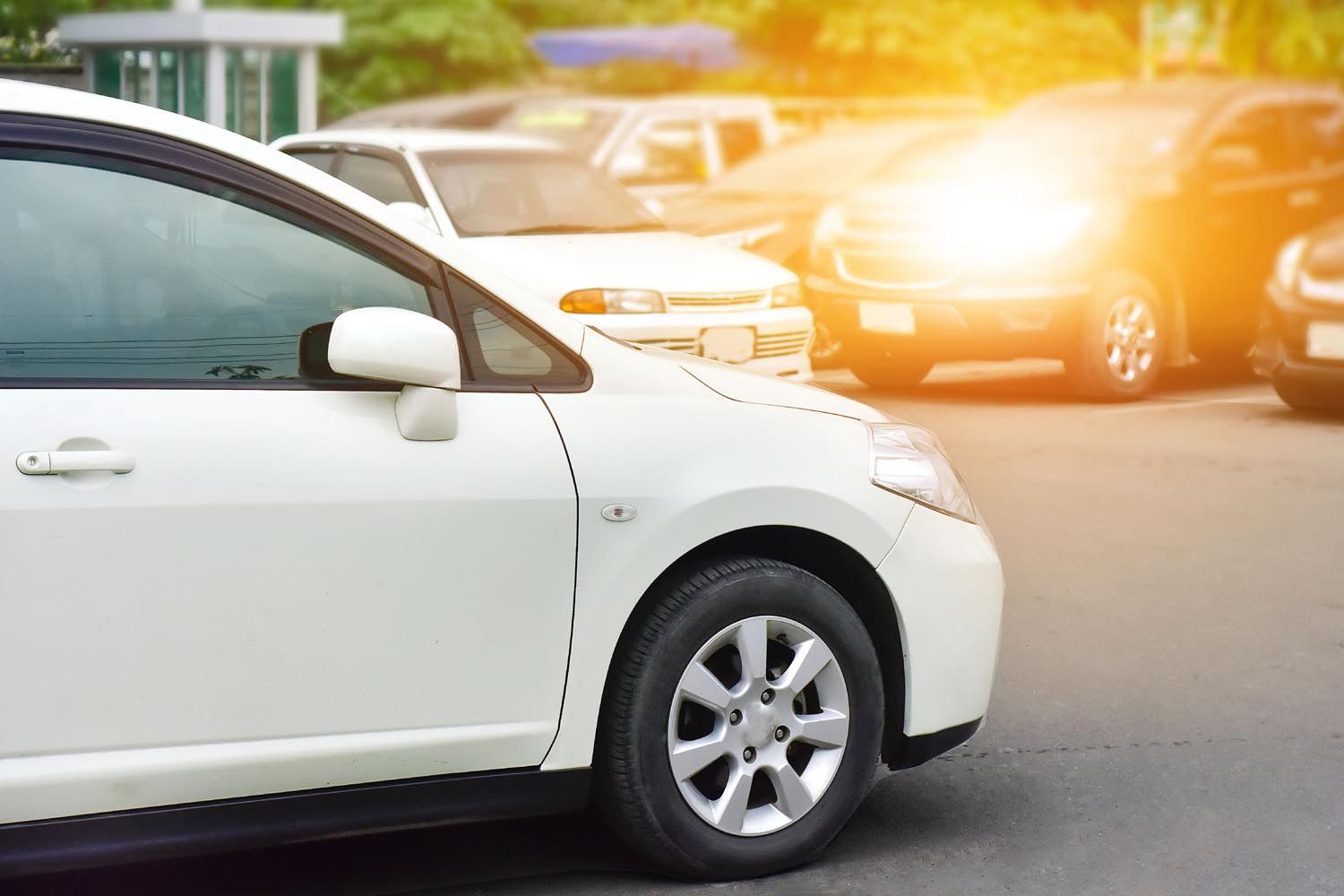 White car in foreground on a street with bright sunlight and blurred traffic in the background
