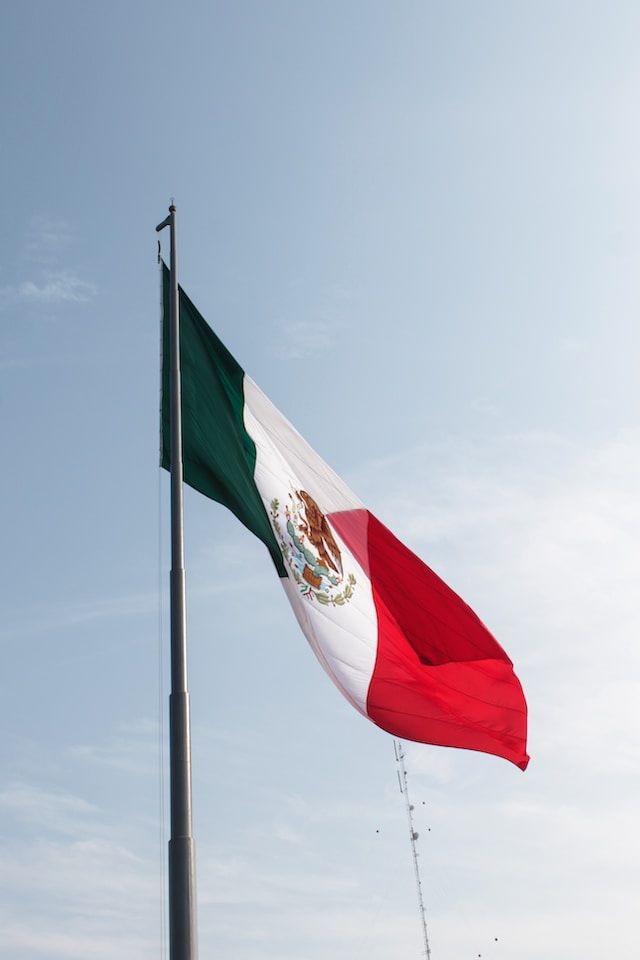 Mexican flag waving on a flagpole against a blue sky