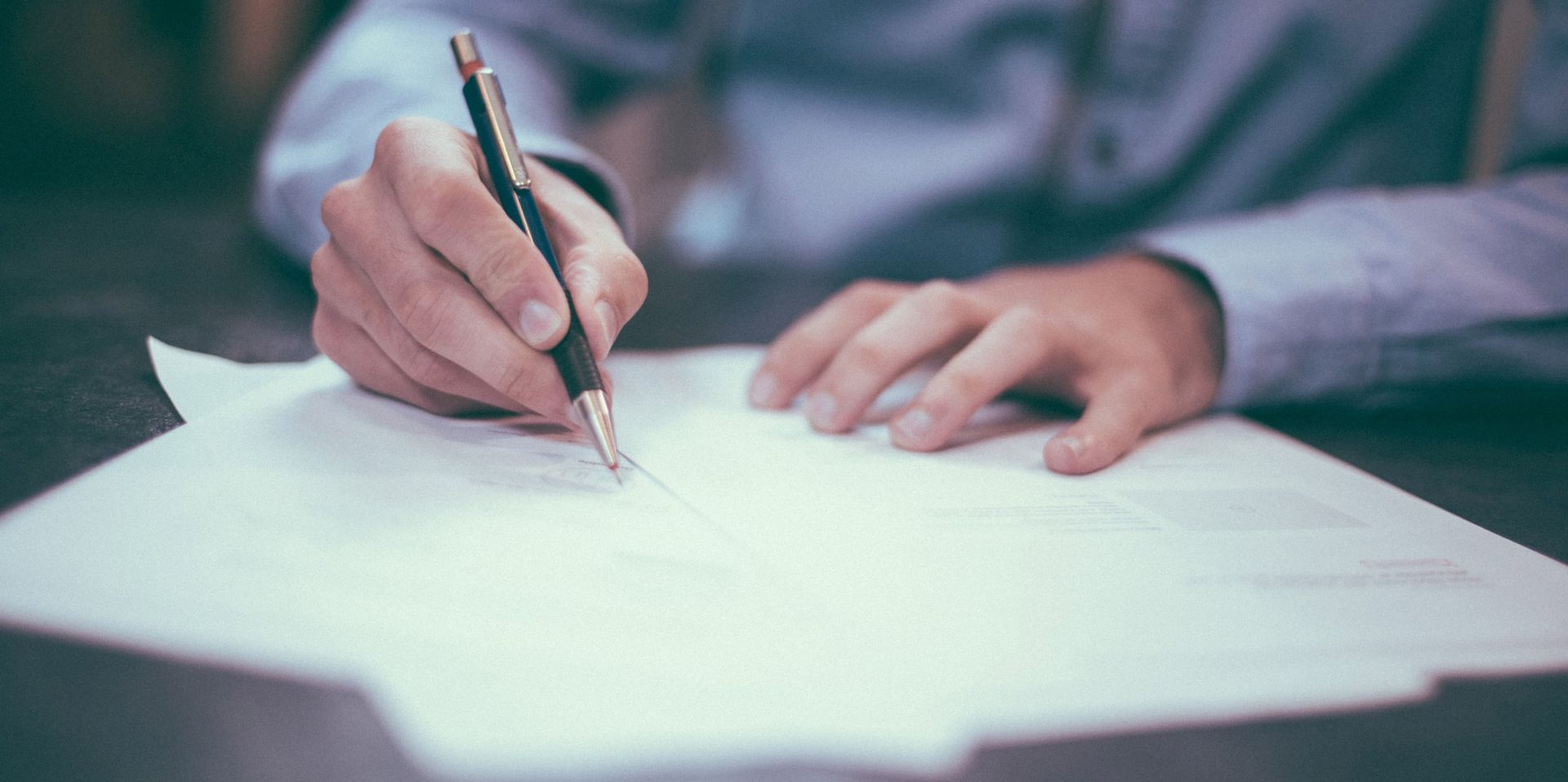 Hand writing on paper with a pen at a desk