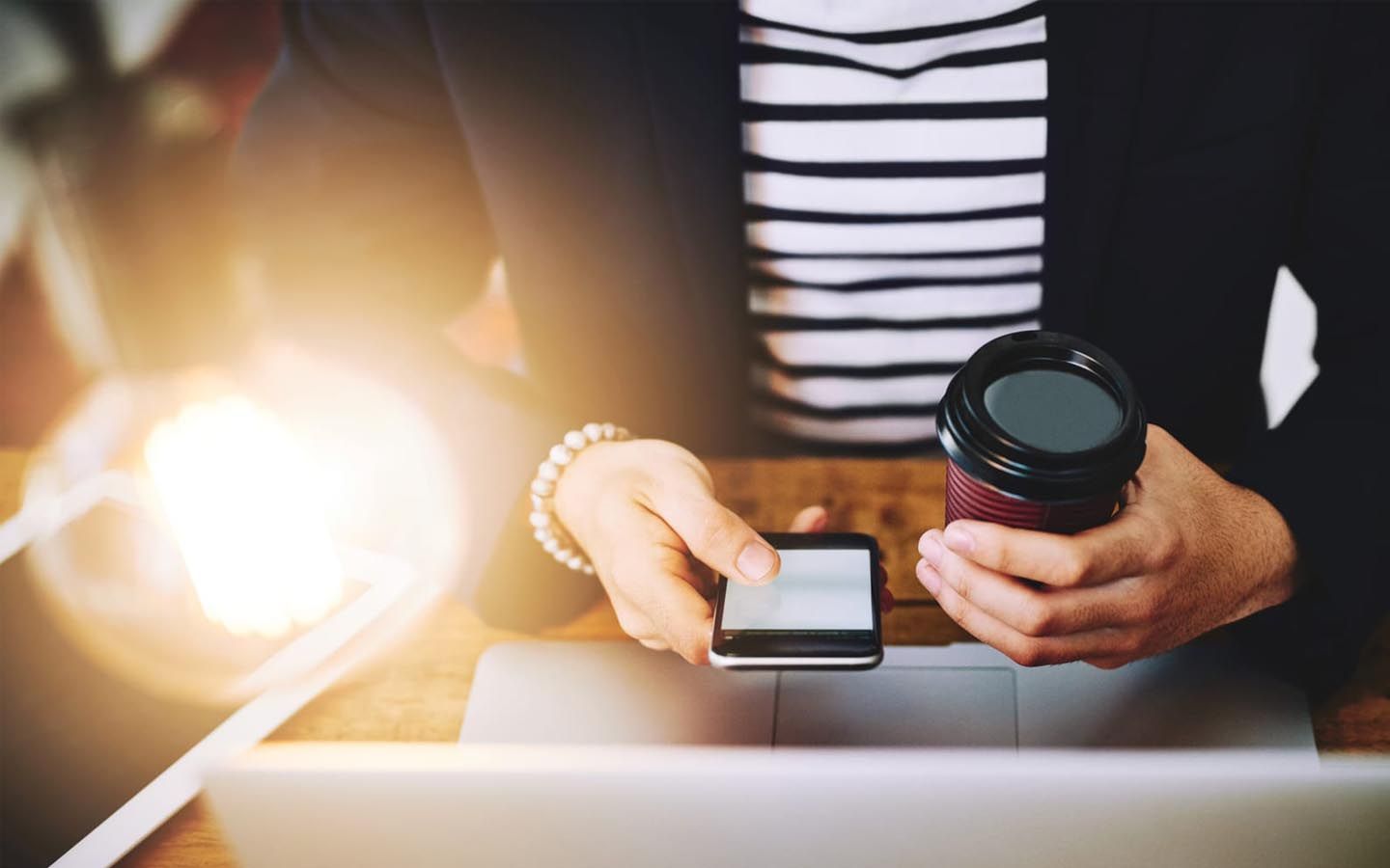 A woman is sitting at a table holding a cup of coffee and reading a mobile phone.