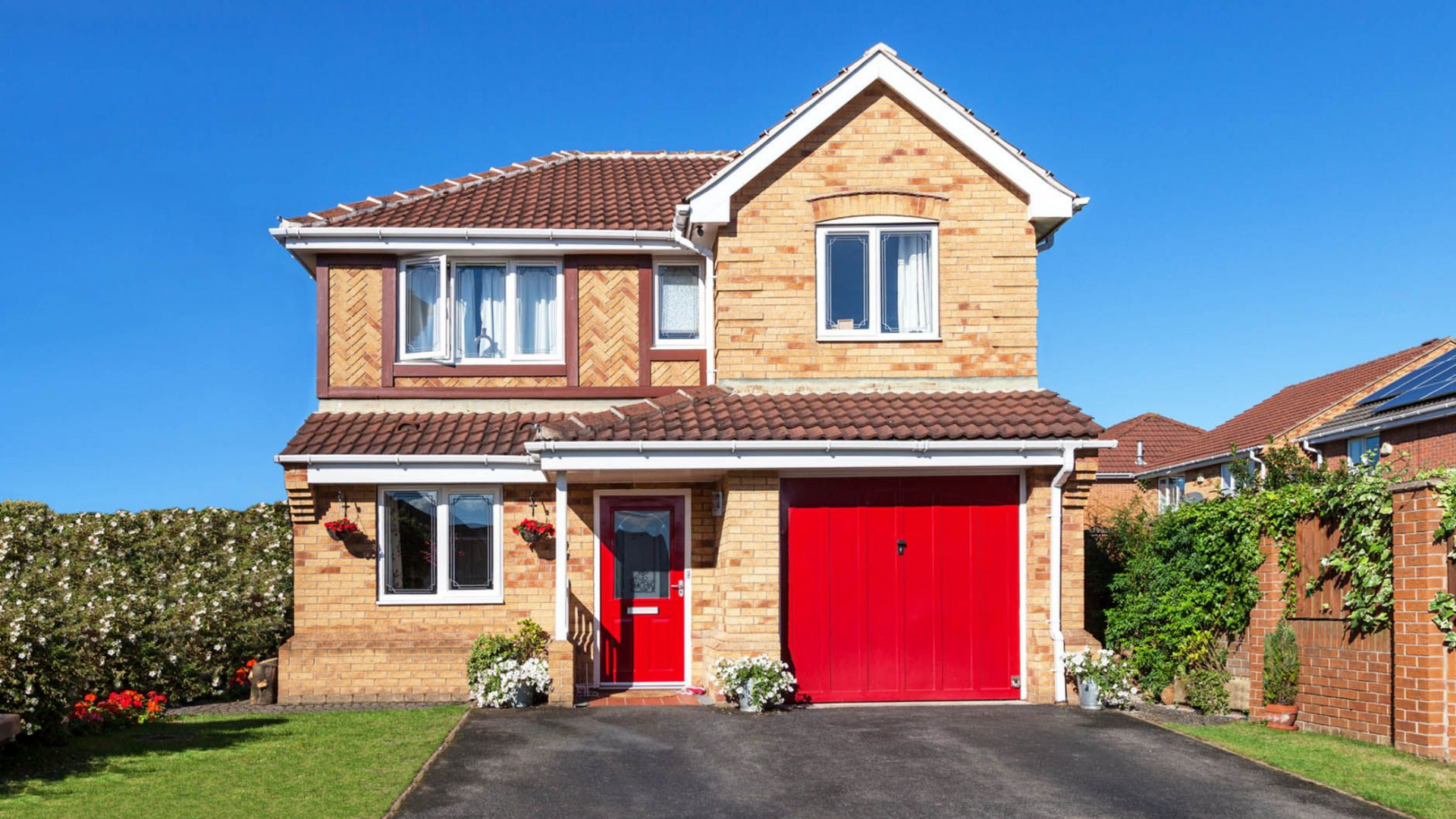 Two-story brick house with a red door and garage against a blue sky.