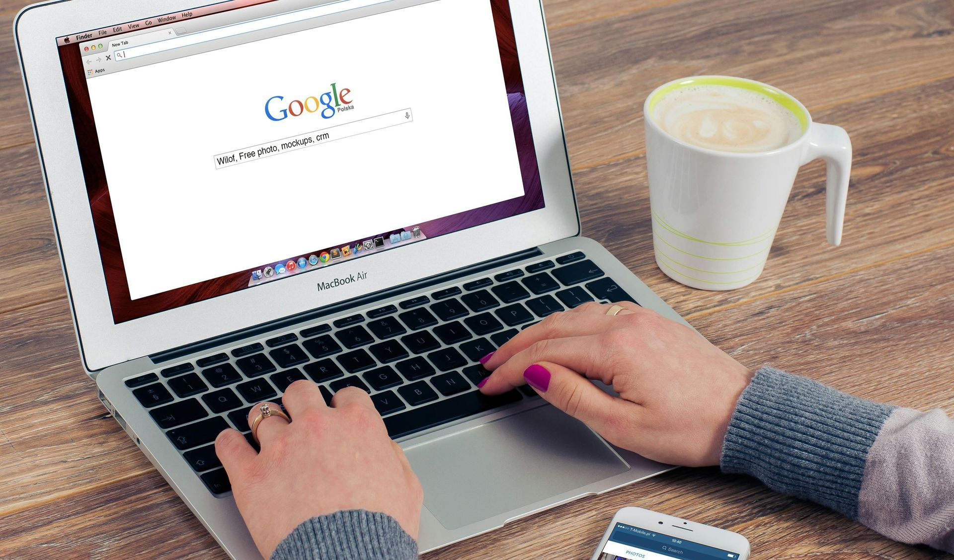 A person is typing on a laptop next to a cup of coffee.
