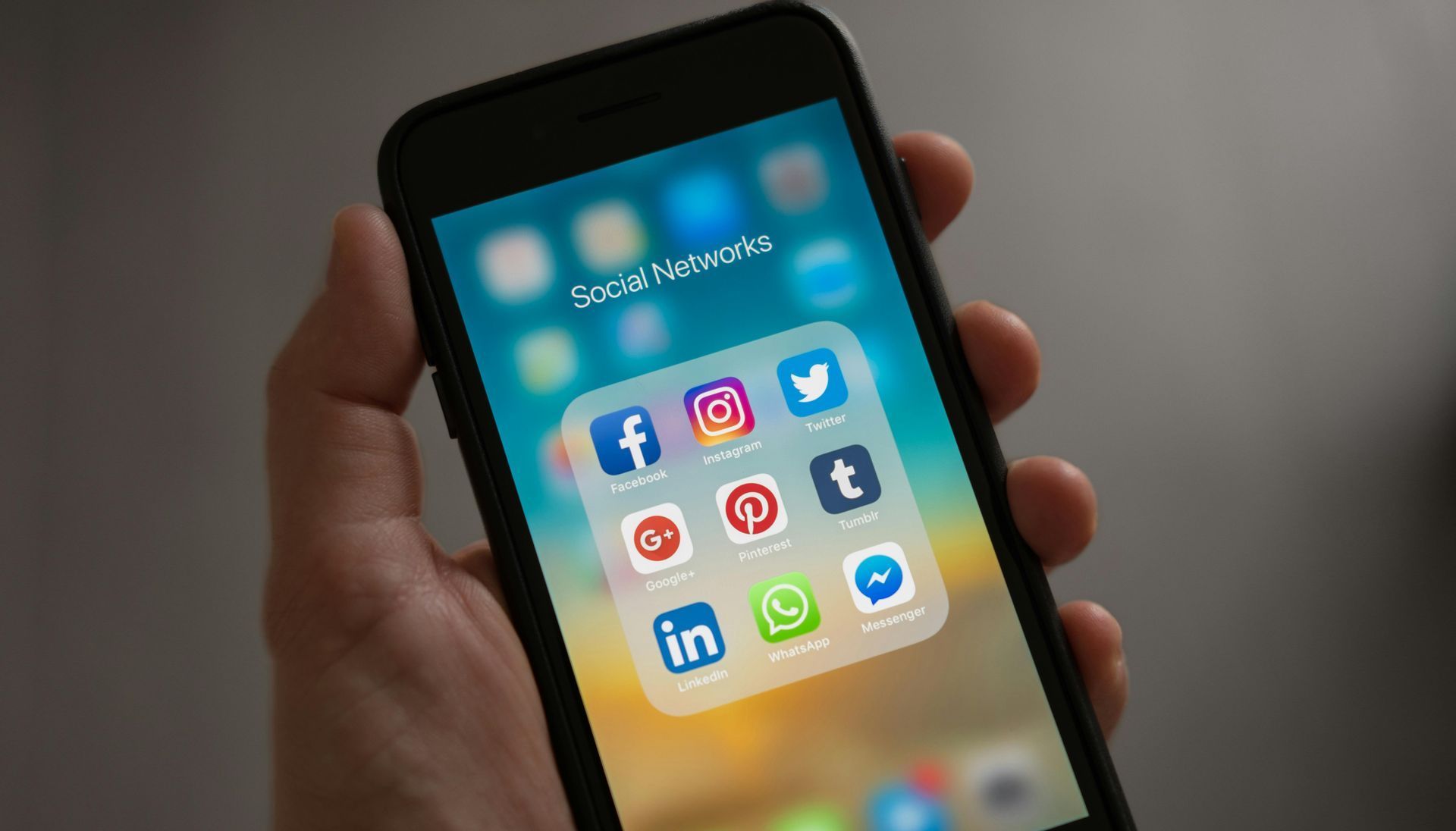 A person is holding a cell phone with social media icons on the screen.