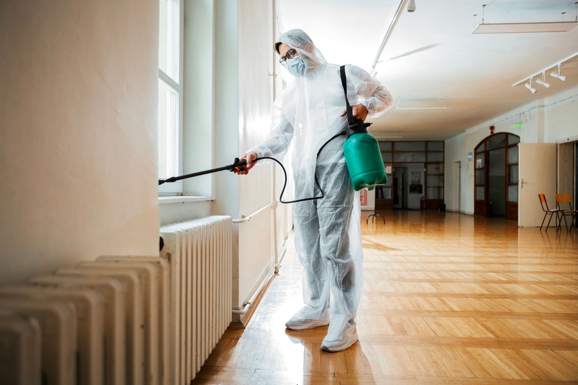 A person in a white protective suit sprays a window, demonstrating local pest control service.