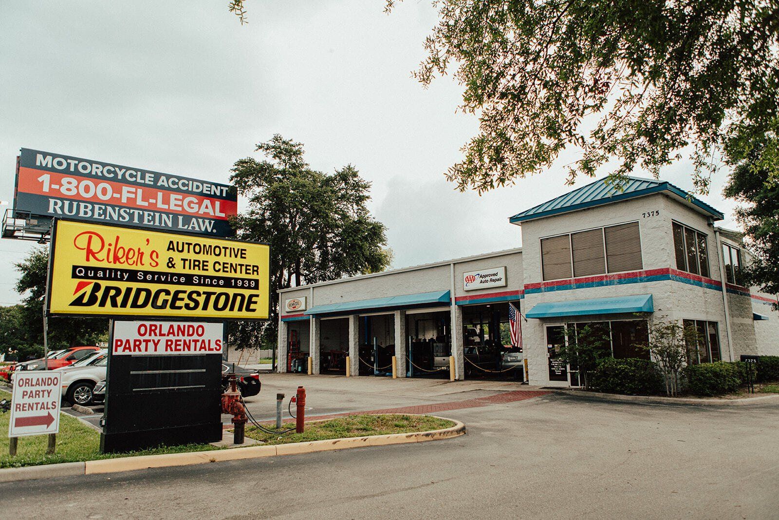 Auto repair shop with Bridgestone sign, motorcycle accident lawyer ad, and a party rental sign. Building has a blue awning.