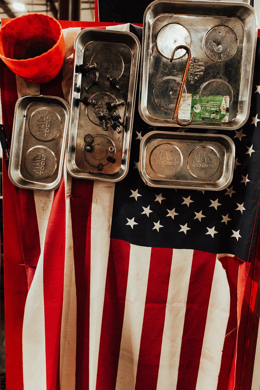 Metal trays holding tools and coins on an American flag, with an orange bucket.