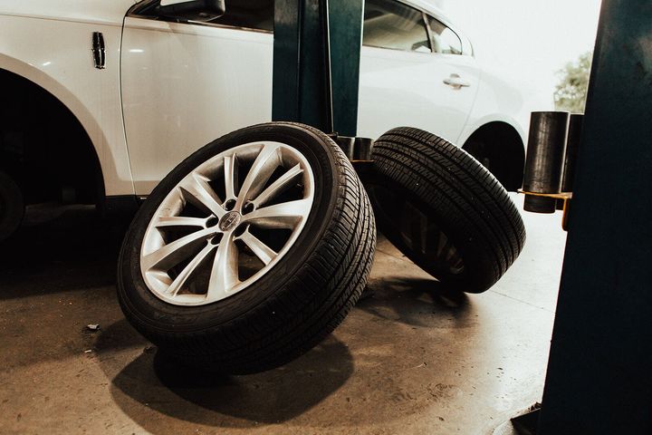 Two car tires with silver rims on a garage floor near a white car.