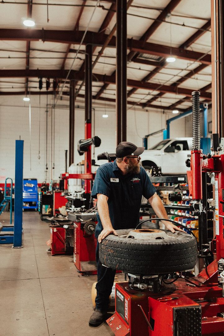 Mechanic holding a tire in a garage, surrounded by equipment, looking off to the side.
