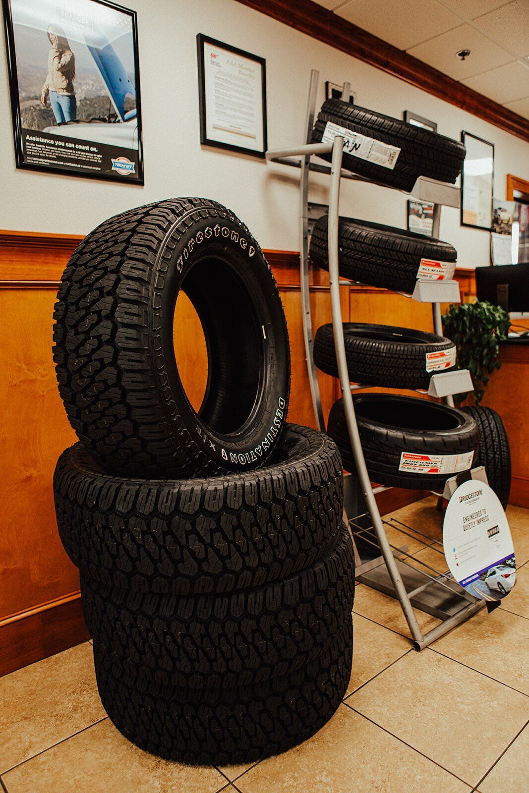 Stack of tires in auto shop, display rack of tires in background.