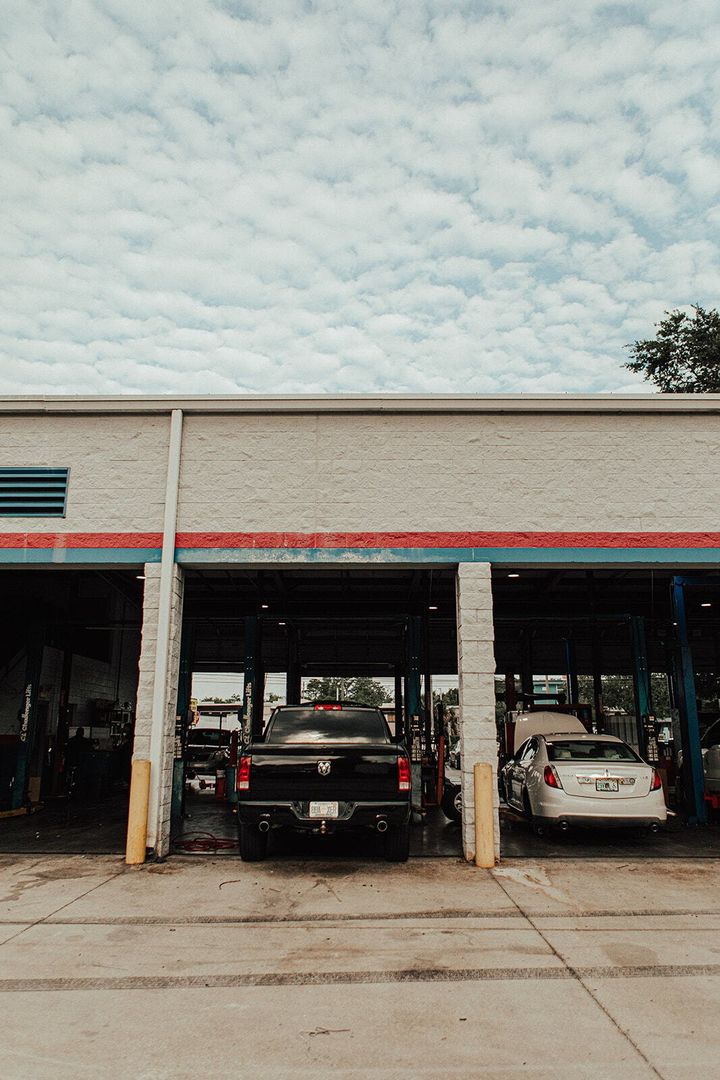 Auto repair shop with three bays, trucks, a car, and a cloudy sky.