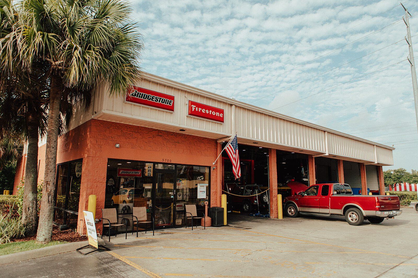 Auto repair shop with red brick facade, red pickup truck, and palm trees. American flag hanging.