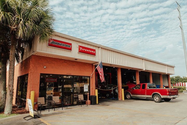 Exterior of a Firestone auto shop with a red truck parked in front. An American flag hangs.