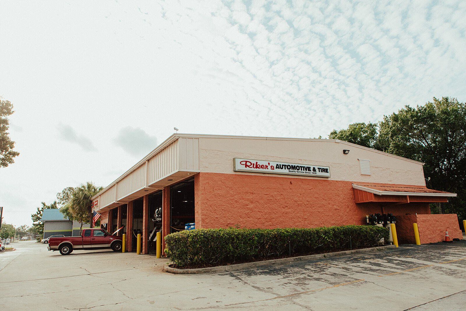 Exterior of a brick building with a business sign, a red truck parked outside, and a cloudy sky.