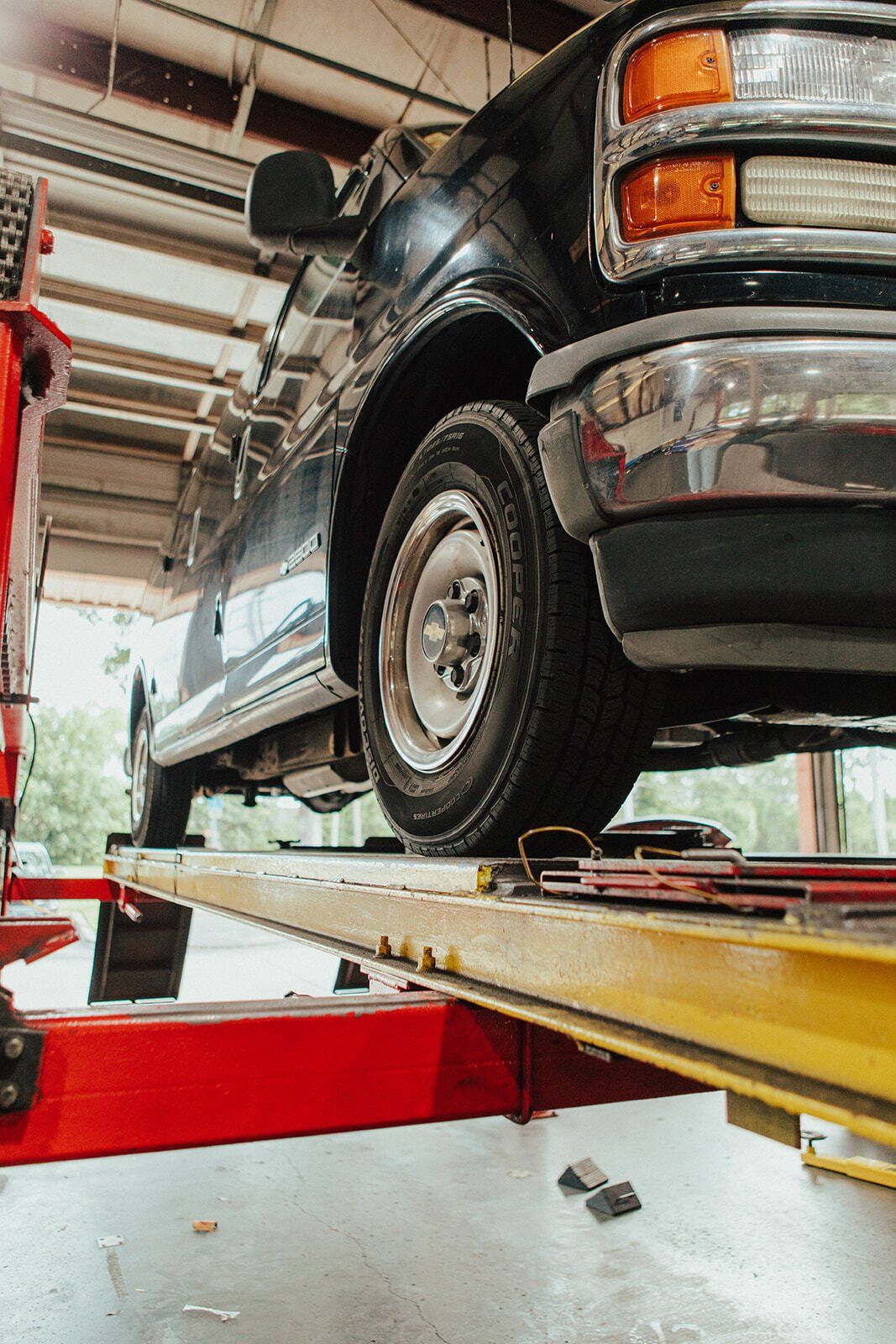 Black truck on a red and yellow car lift inside a garage; tire, bumper and headlight are visible.