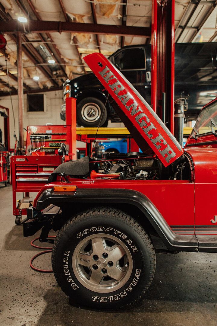 Red Jeep Wrangler with hood up in a garage, next to a car lift. 