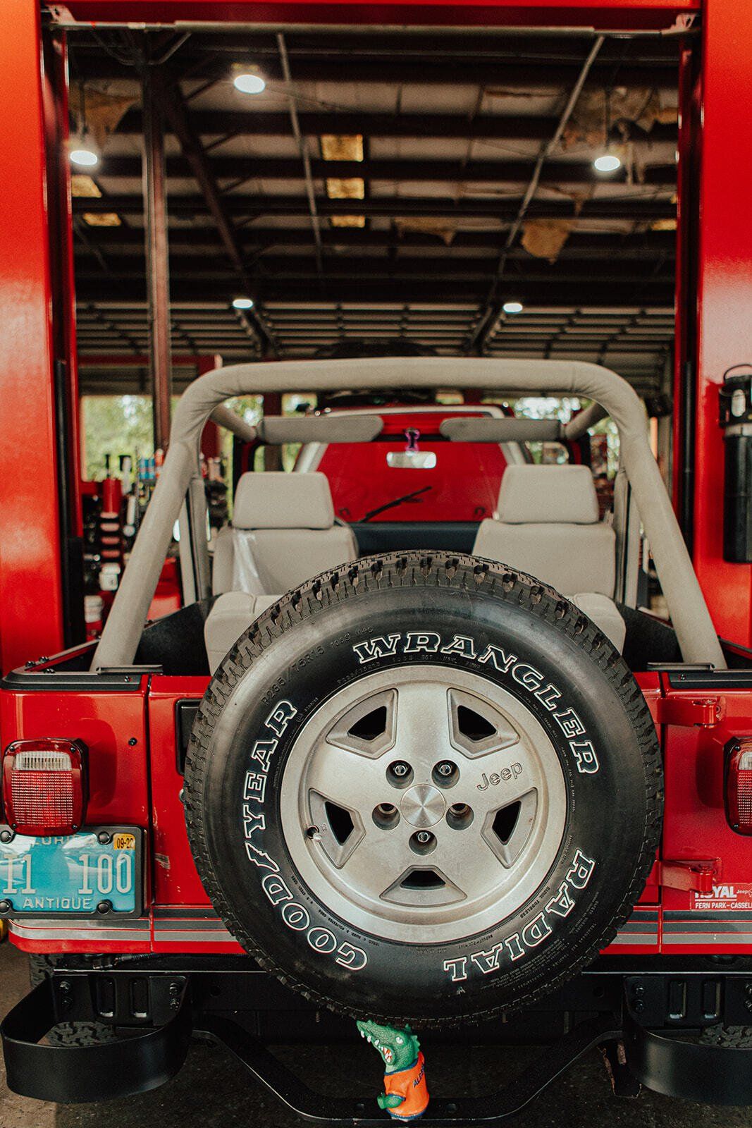 Red Jeep Wrangler rear view, spare tire, roll bar, inside a building.