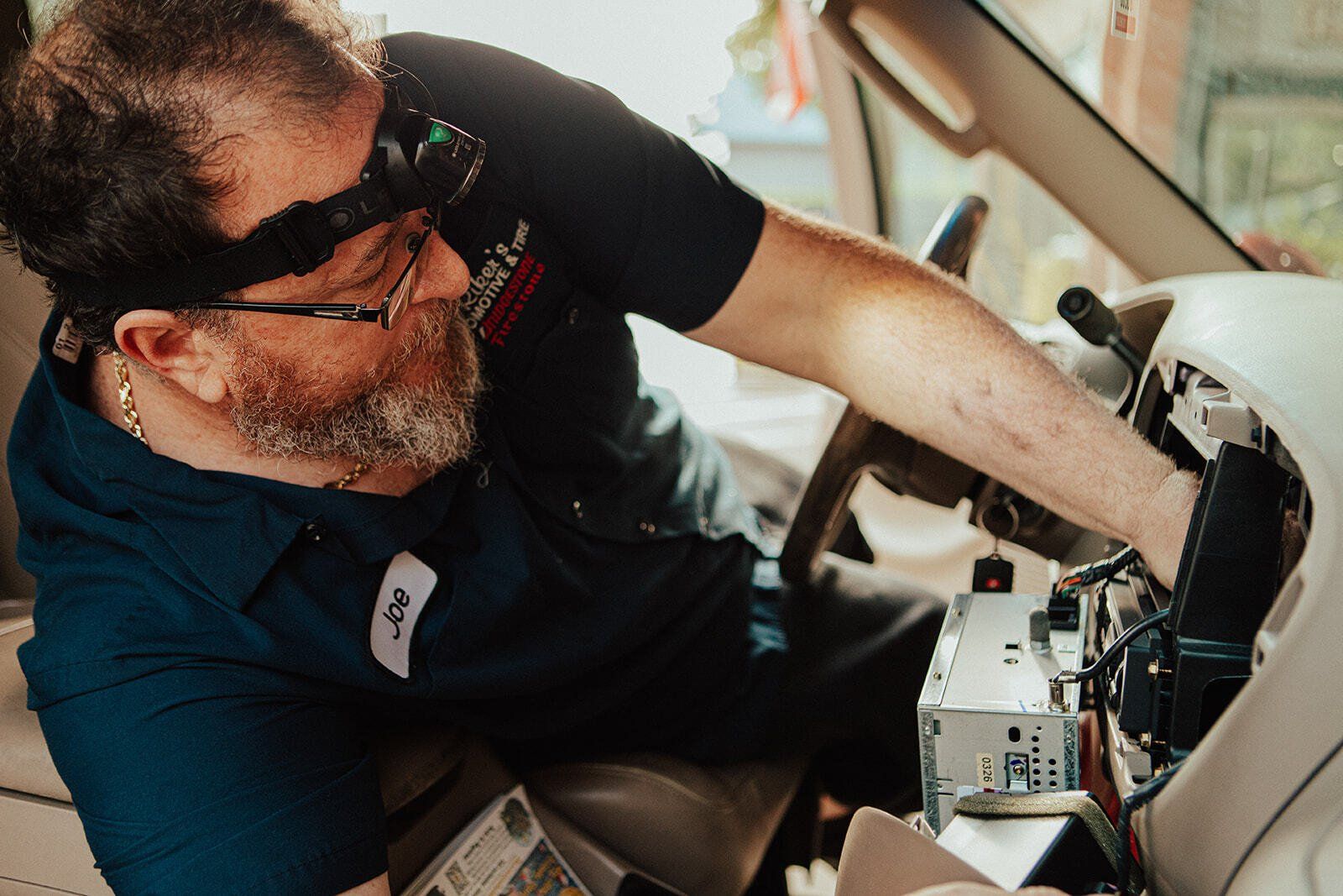 Mechanic working on car dashboard, wearing a headlamp.