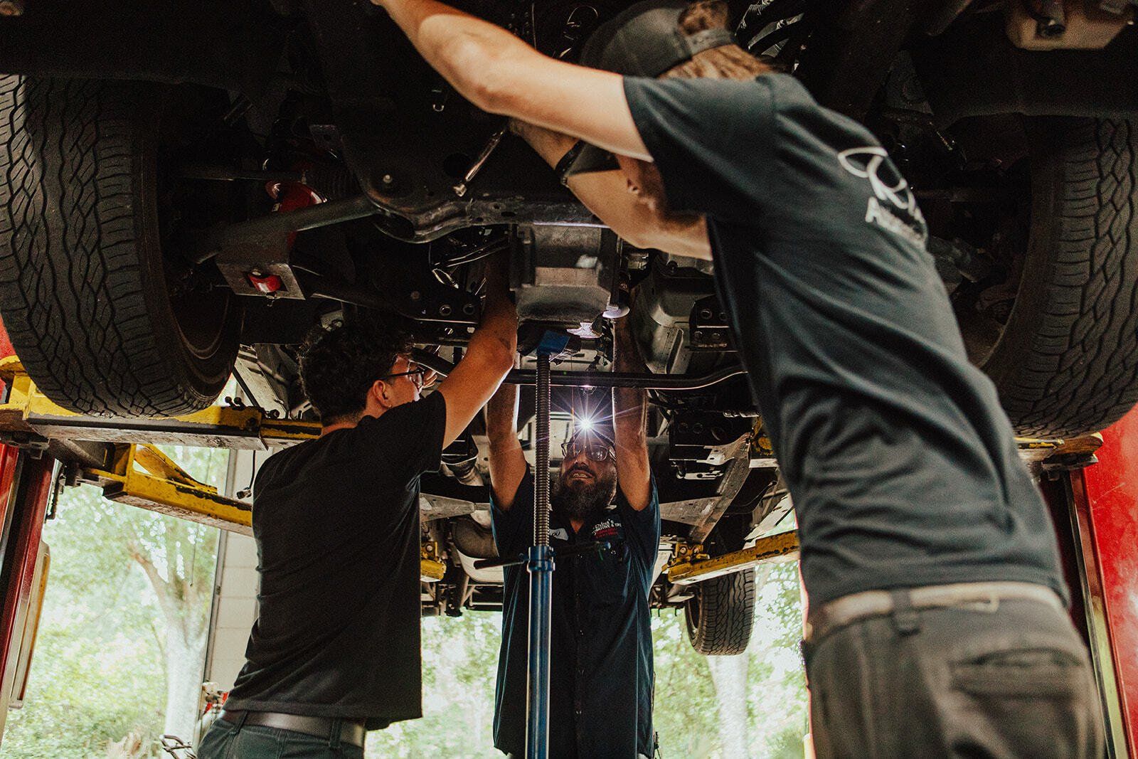 Three mechanics working under a raised vehicle in a garage.