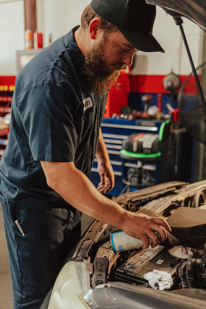 Mechanic in blue uniform working on car engine, inspecting parts. Auto shop setting.