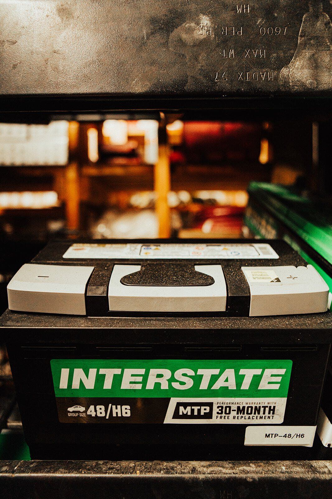 Black Interstate car battery on a shelf, with a green and white label visible.