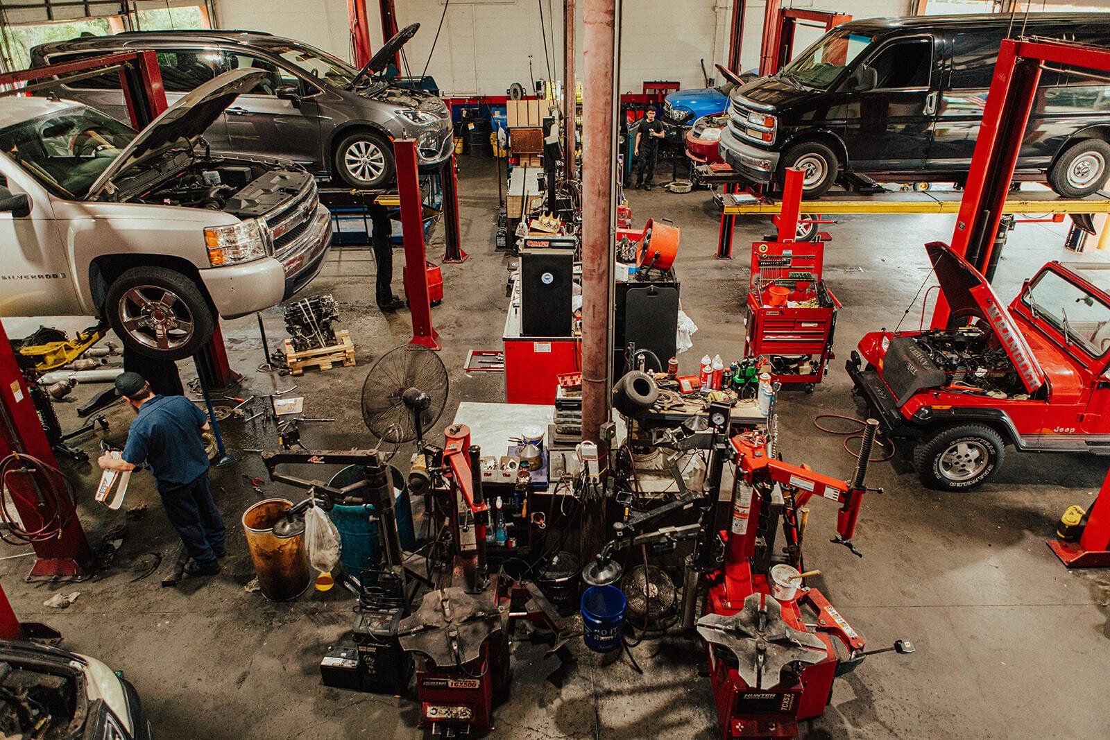 A cluttered auto repair shop with multiple cars on lifts and mechanics working on vehicles.