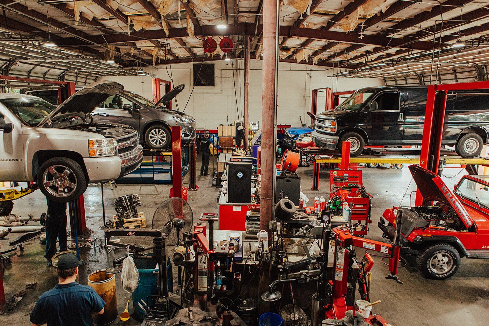 Cars on lifts in a busy auto repair shop, mechanics working among tools and equipment.
