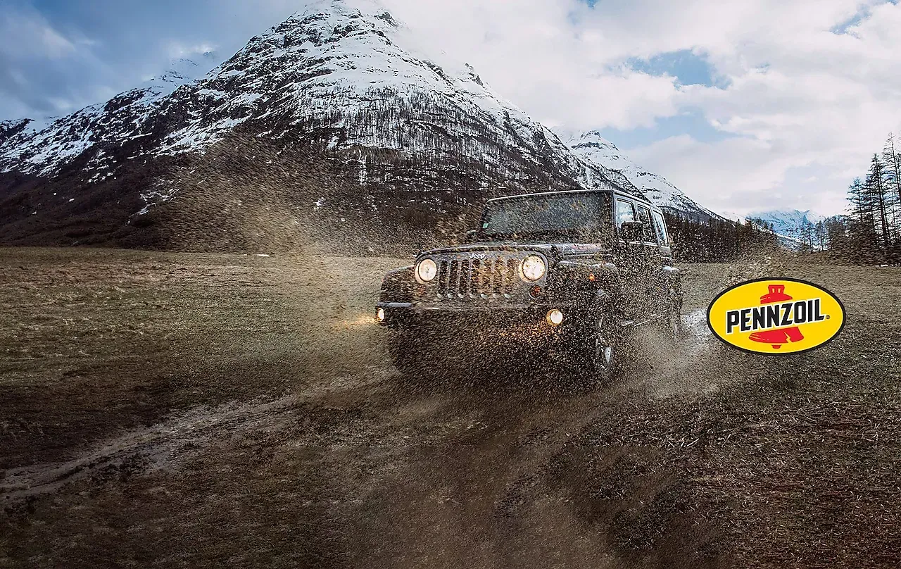 Jeep splashes through muddy terrain, with snowy mountain in the background. Pennzoil logo in corner.