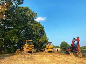 Two bulldozers and an excavator are parked in a dirt field.