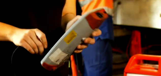 Person holding a device with a cable, likely for testing or measurement, possibly in a work environment.
