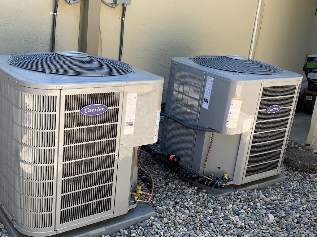 Two air conditioners are sitting on top of a pile of gravel.