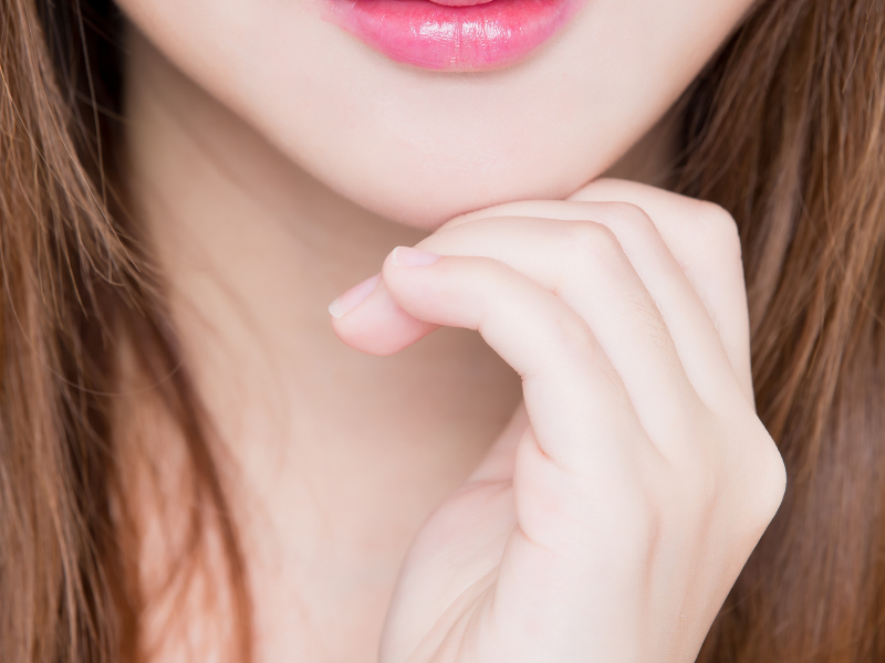 Close-up of a person with pink lipstick, fair skin, and long brown hair, resting their chin on their hand.