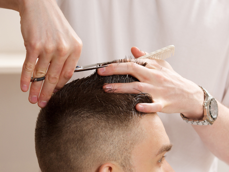 Hands of a barber cutting a man's hair with scissors and comb. The man is seated in a salon chair.