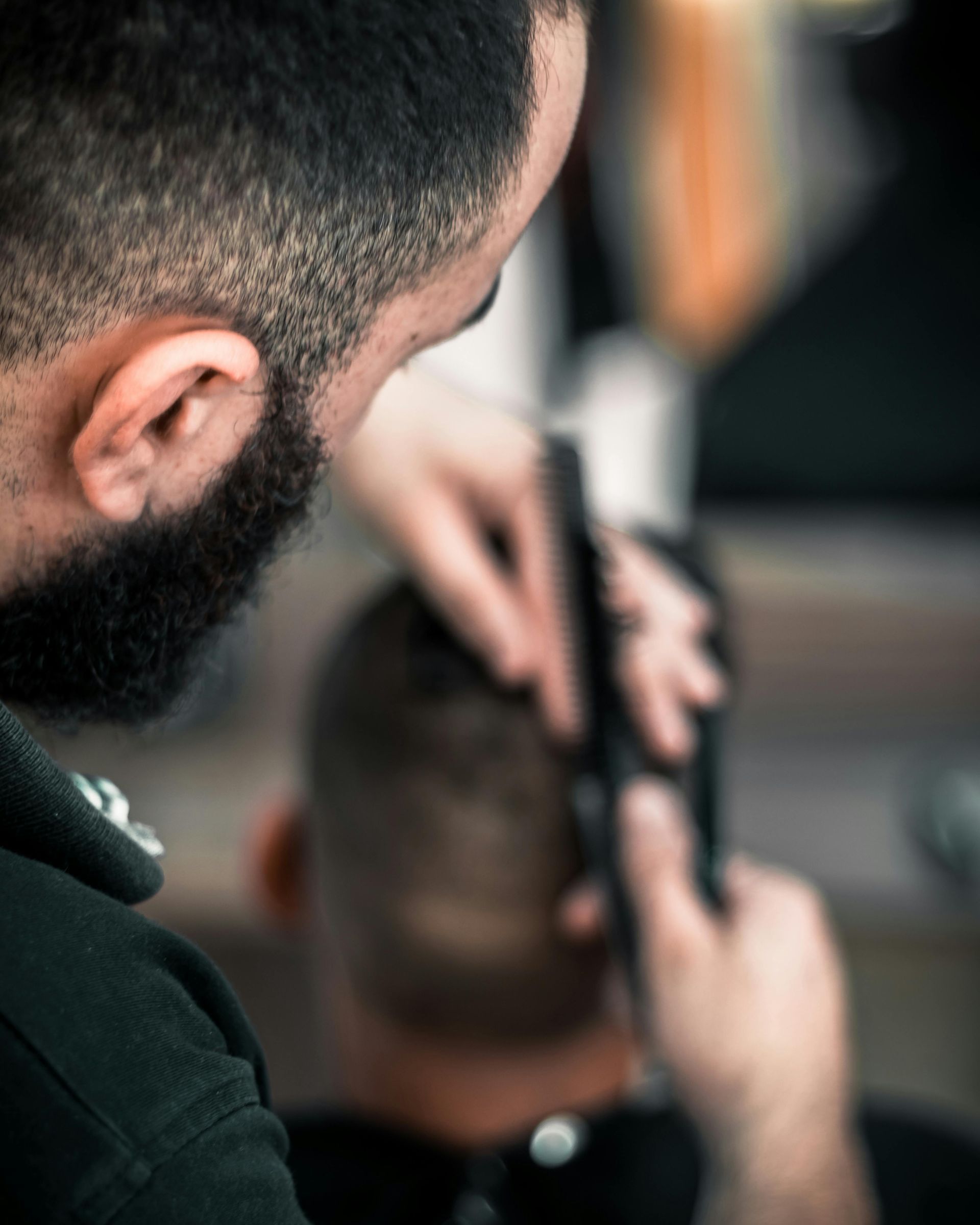 Barber giving a haircut with clippers. Close-up shows the barber's face and hands, and the client's head.