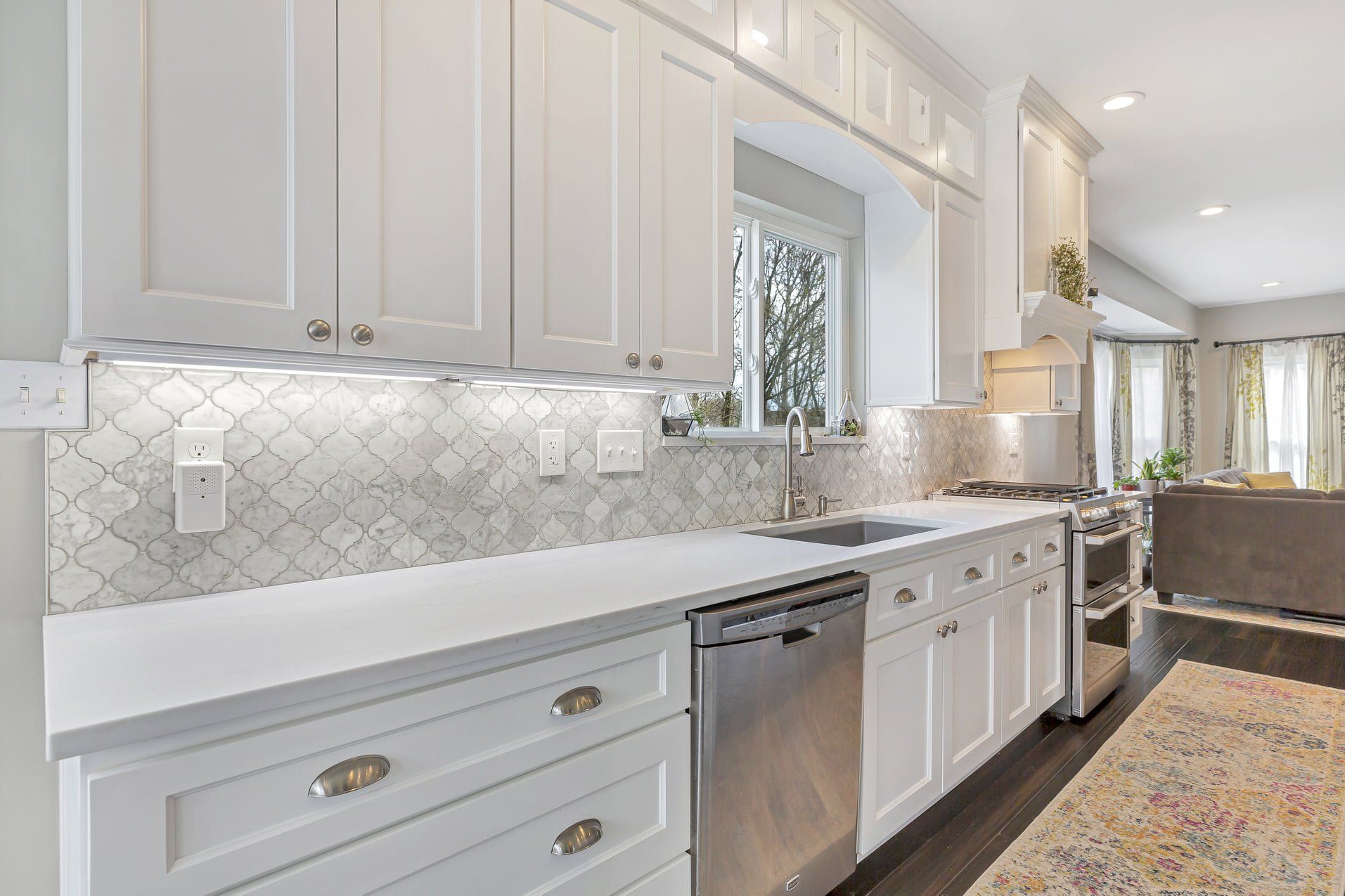 Bright modern kitchen with white cabinets, gray backsplash, and stainless dishwasher.