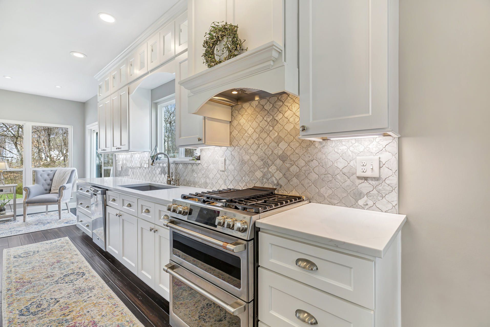 Bright white modern kitchen with marble counters, stainless steel stove, and patterned backsplash